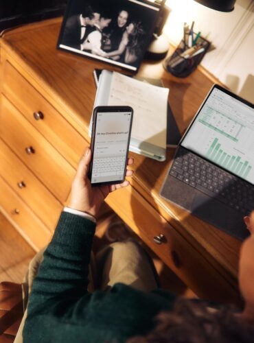 Person holding phone near laptop and tablet on desk